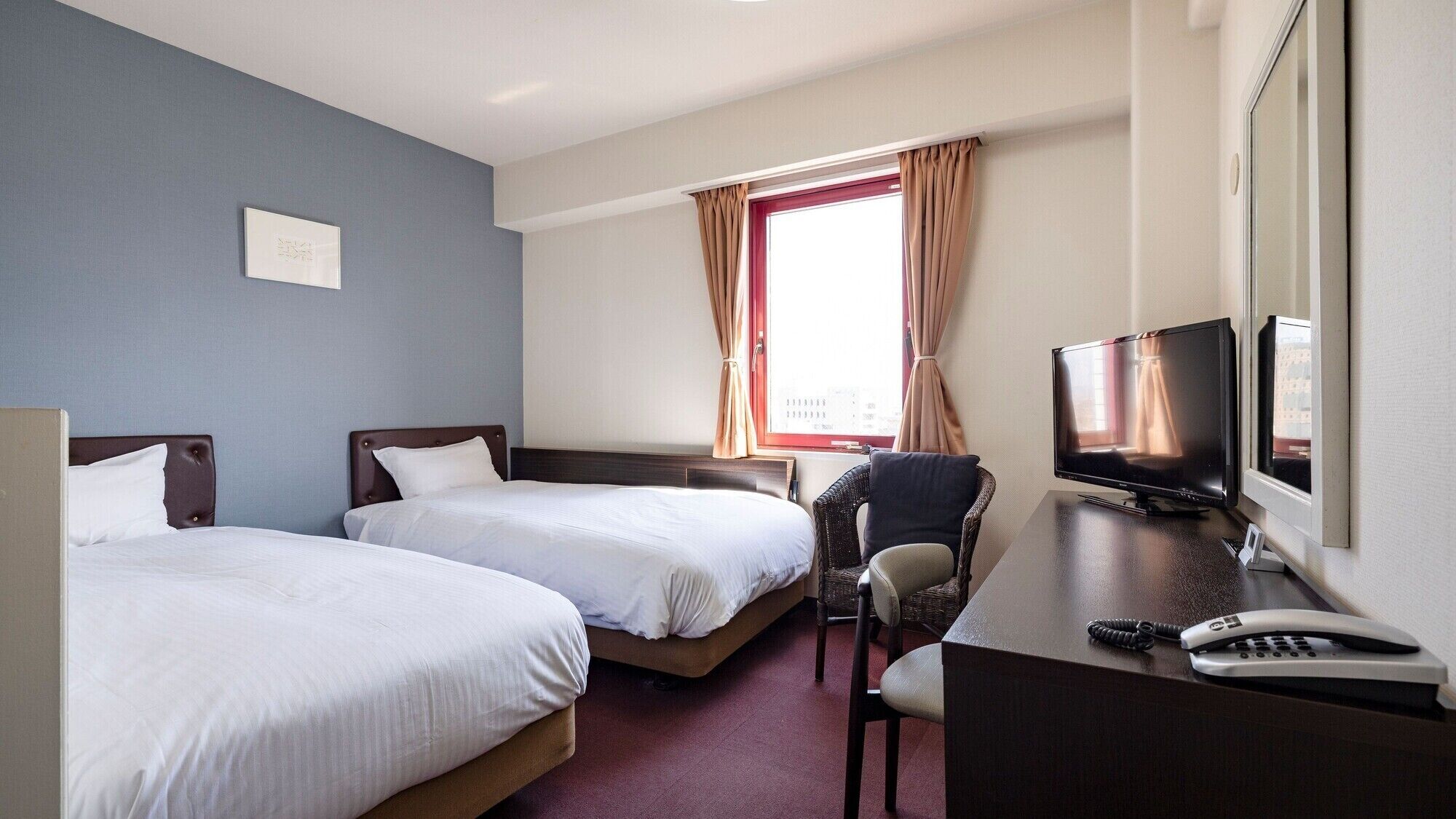 Une chambre d’hôtel avec deux lits, un bureau avec une télévision et une chaise.