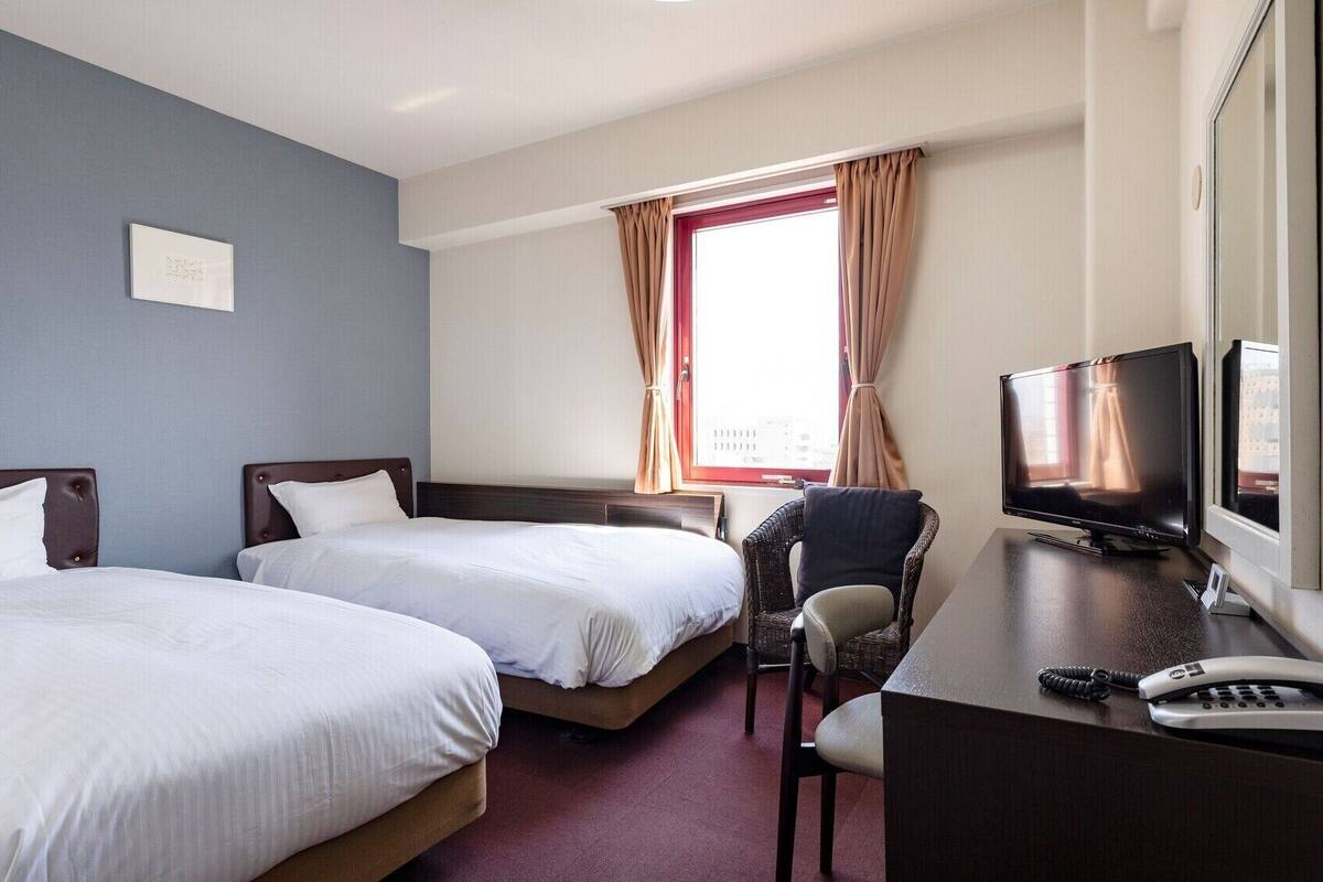 Habitación de hotel con dos camas, un escritorio con televisor y una silla.