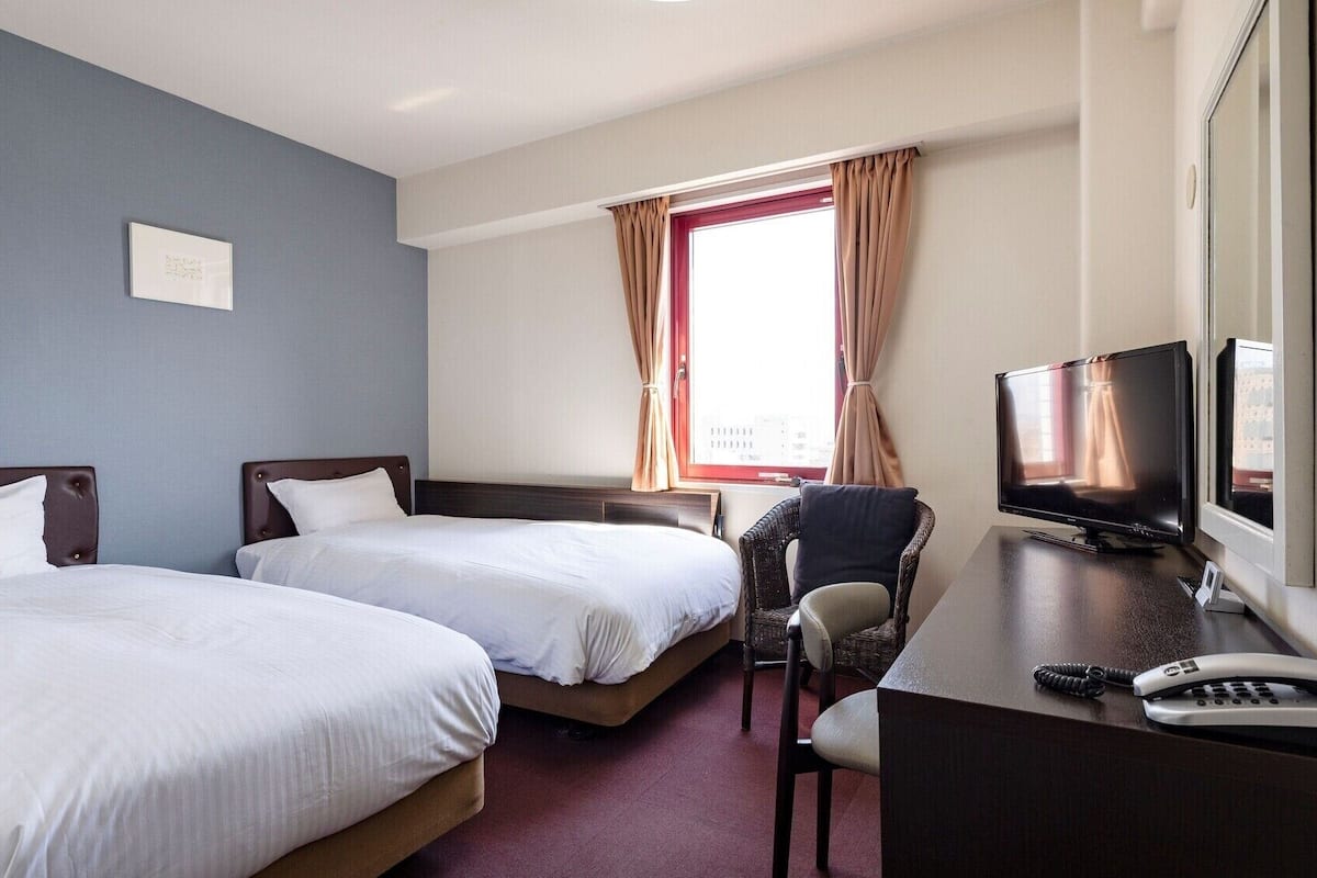 A hotel room with two beds, a desk with a TV, and a chair.