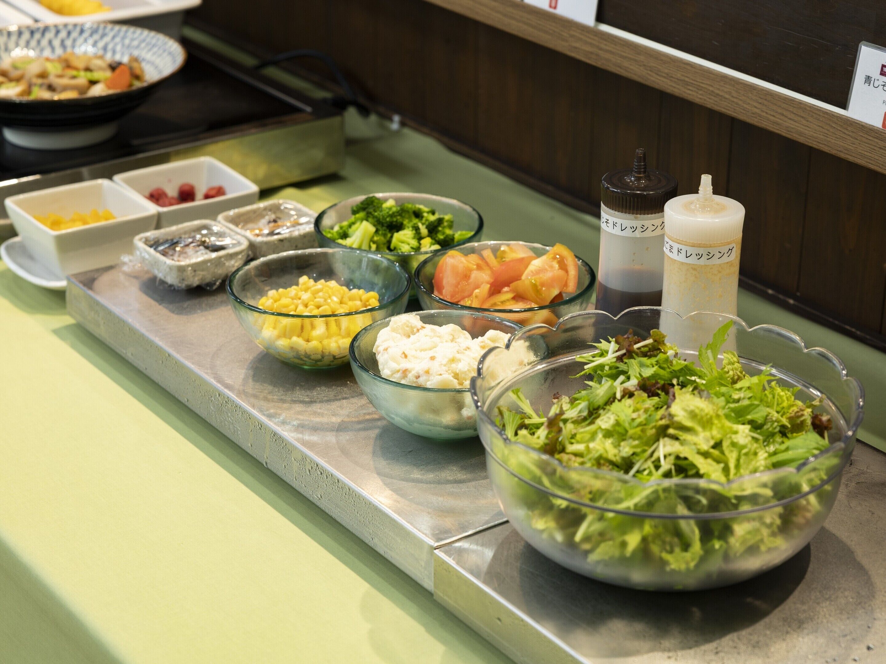 A buffet table with various food items including corn, broccoli, and salad.