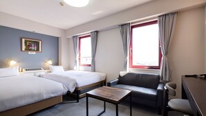 Quarto de hotel com duas camas, uma escrivaninha, uma cadeira e janela com cortinas.