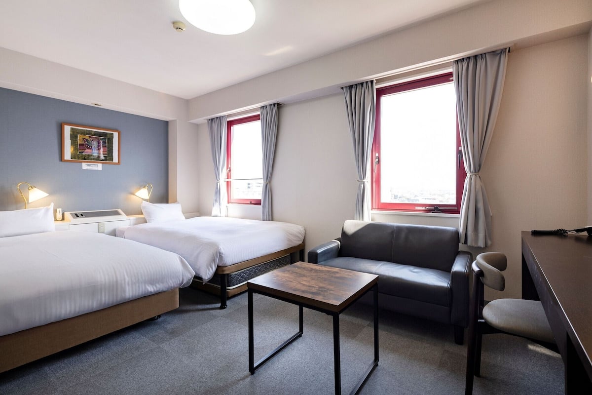 Habitación de hotel con dos camas, un escritorio, una silla y una ventana con cortinas.