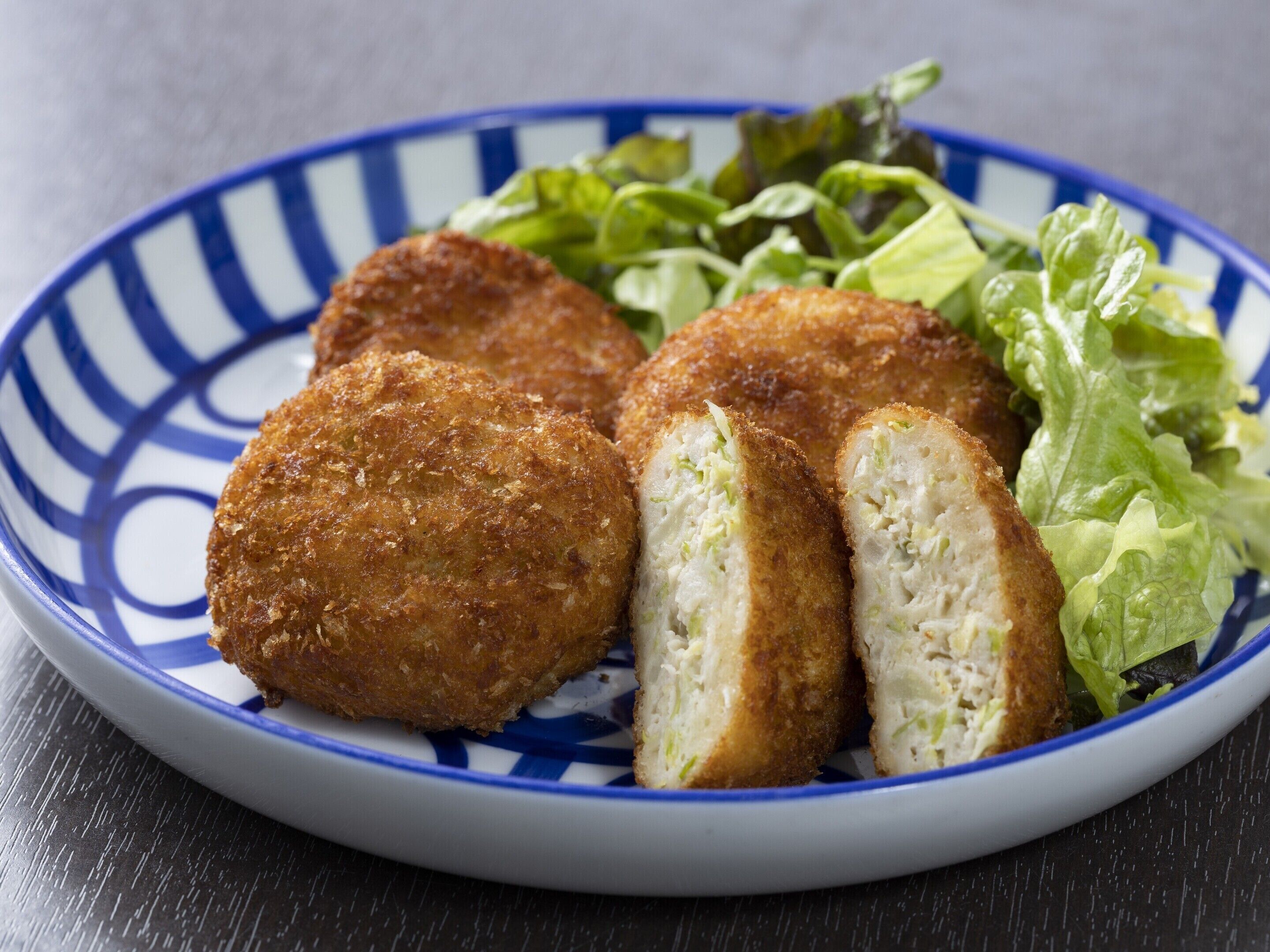 Un plato con croquetas y una ensalada como guarnición sobre un plato azul y blanco estampado.