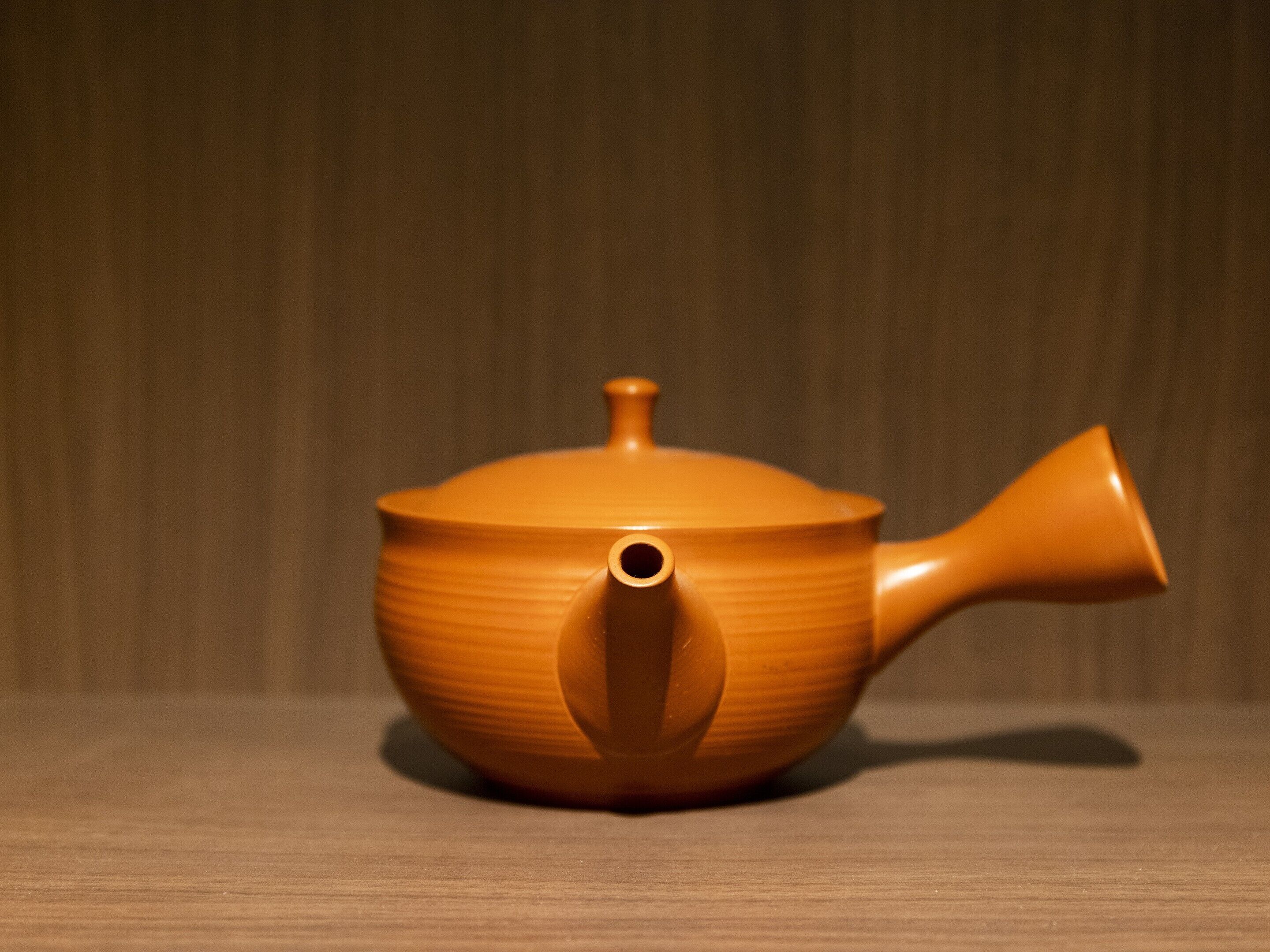 A ceramic teapot with a spout and handle, placed on a wooden surface.