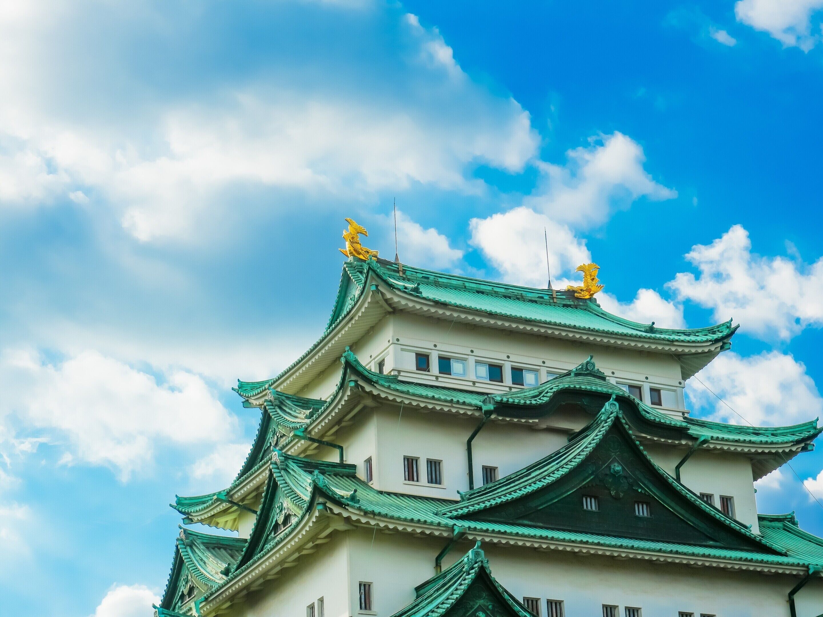 Un castillo japonés tradicional con varios niveles y techos verdes, sobre un cielo parcialmente nublado.