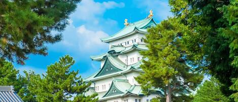Um castelo japonês tradicional com vários níveis e telhados verdes, rodeado por árvores verdes exuberantes.