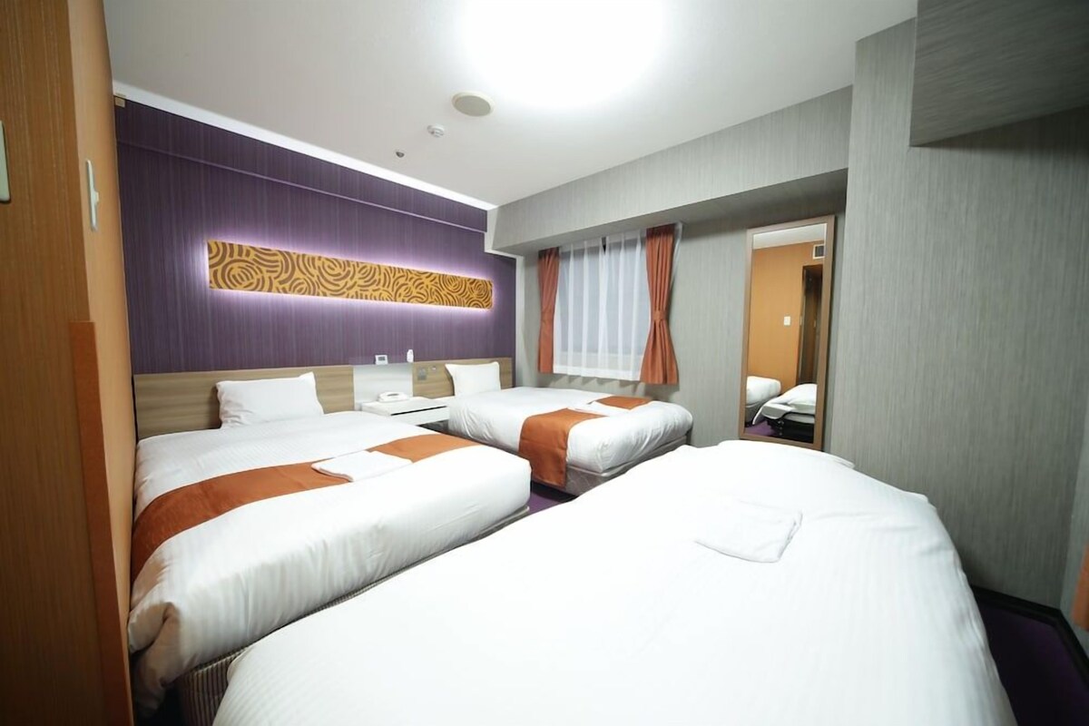 Une chambre d’hôtel avec deux lits, un luminaire fixé au mur, un miroir et une fenêtre avec des rideaux.