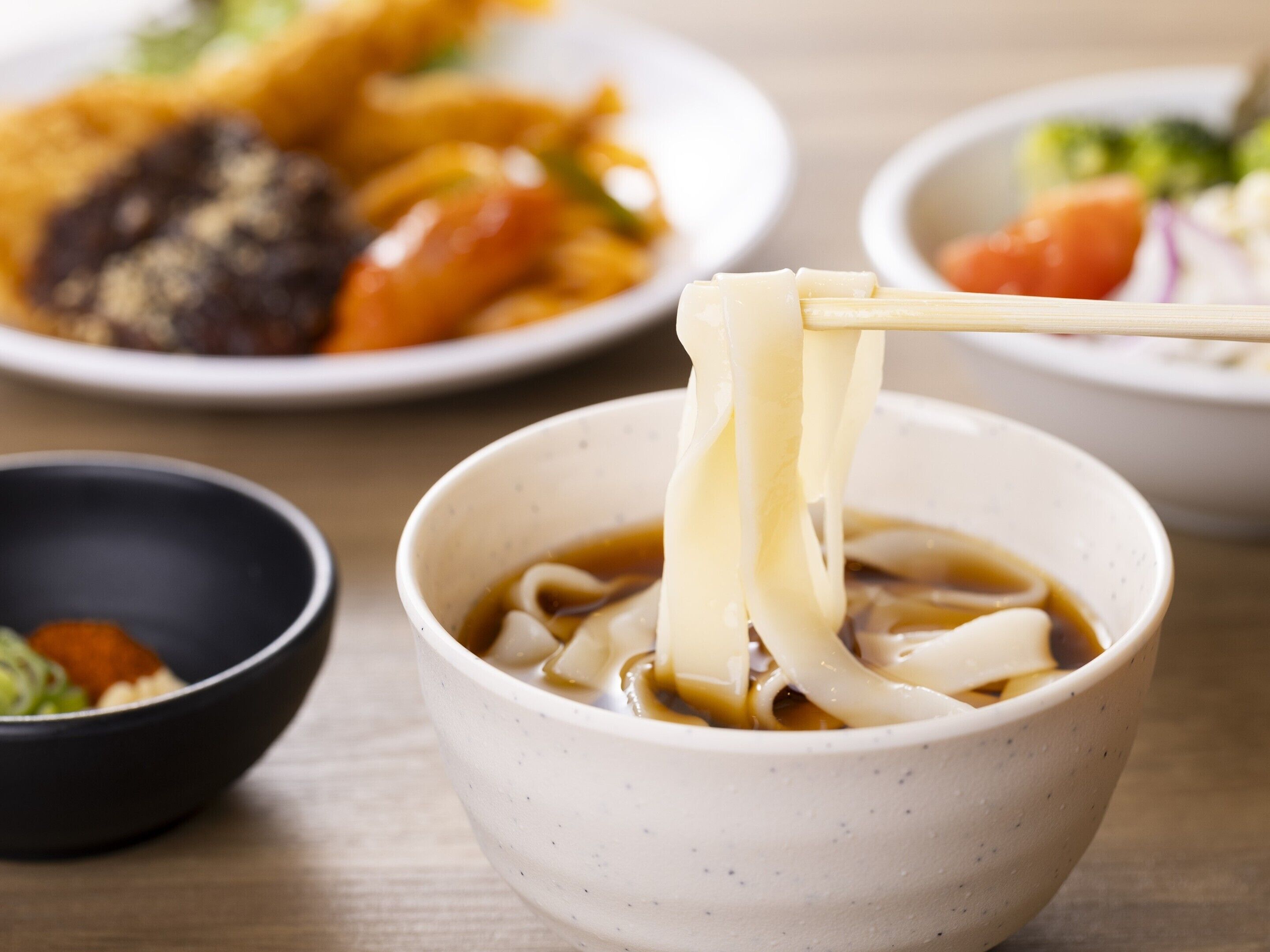 Eine Schüssel mit Ramen-Nudeln wird mit Stäbchen angehoben.