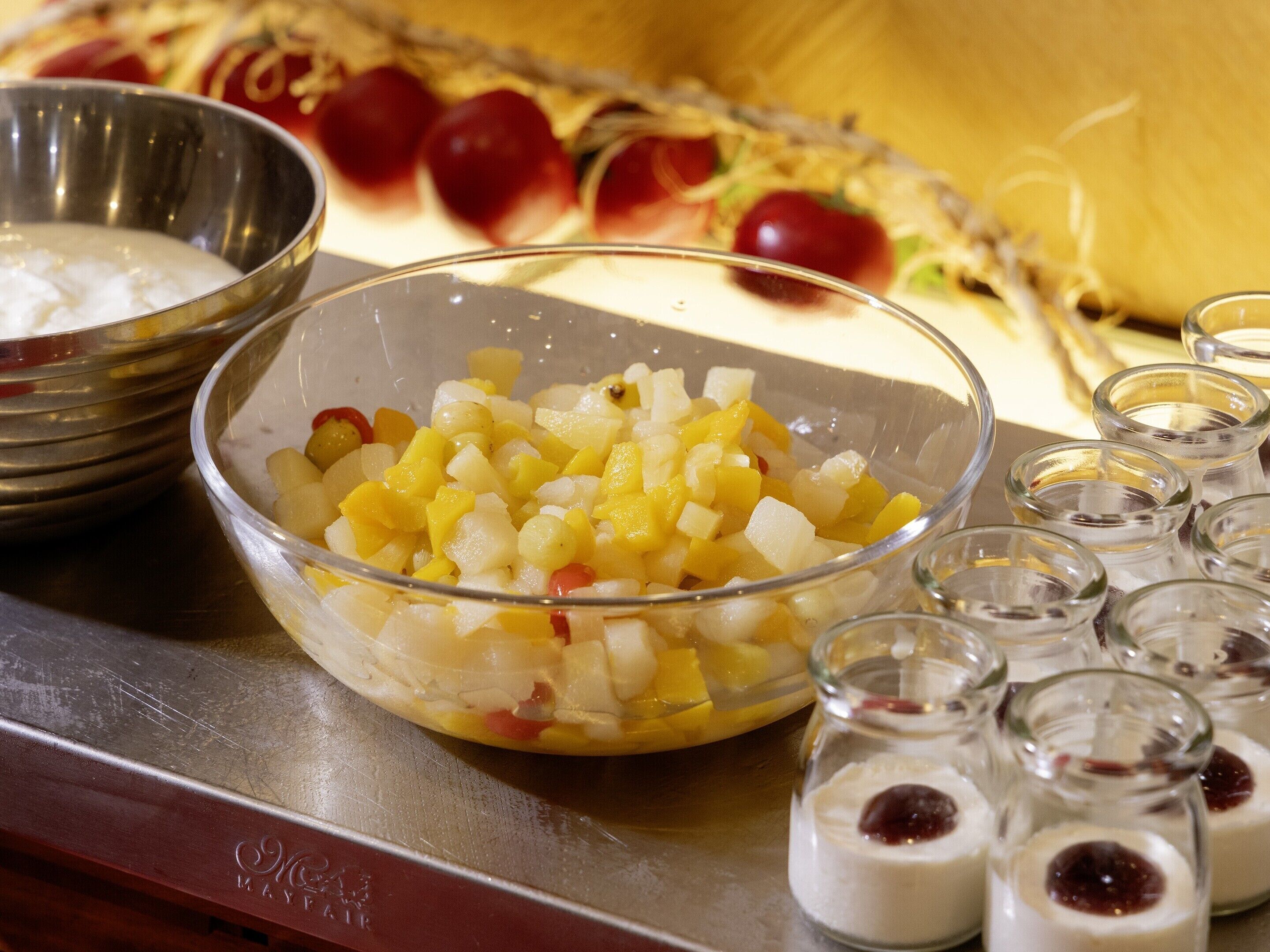 Un bol de fruits coupés en dés, un bol en métal et de petits pots en verre contenant une substance blanche.