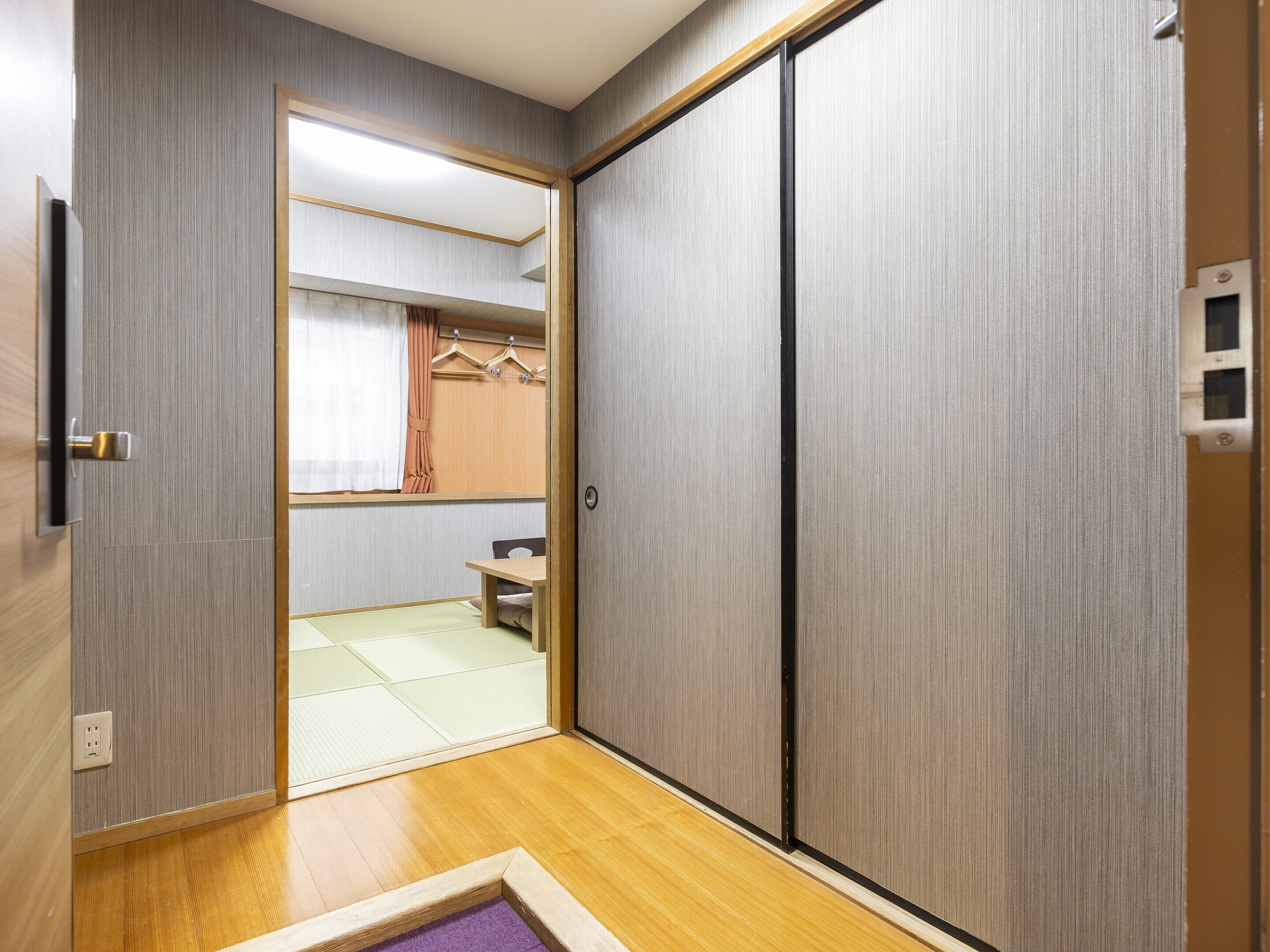 A room with a sliding door leading to a bathroom, a wooden floor, and a small table with a chair.