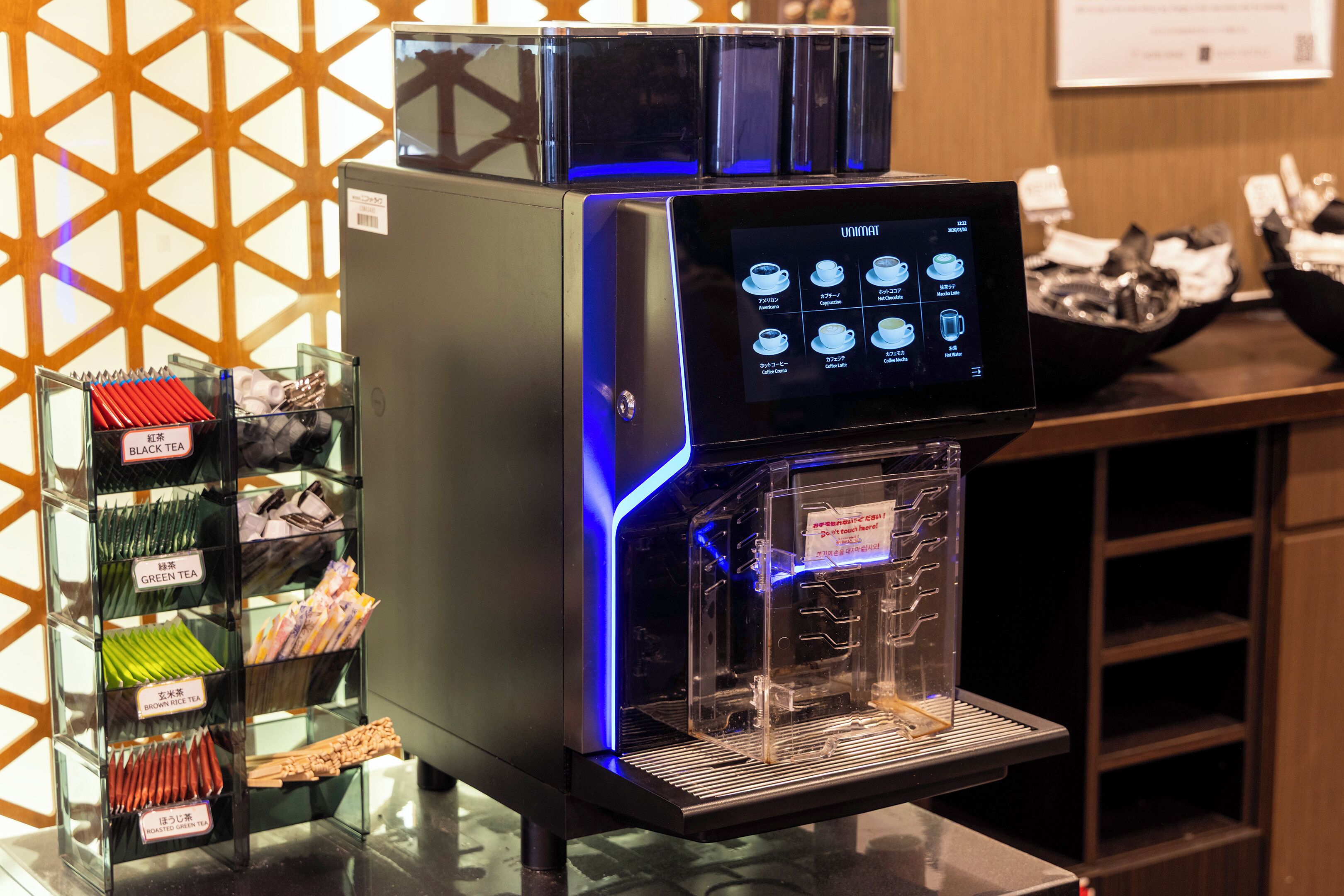 A coffee machine with a digital display, a glass display case with tea packets, and a wooden counter.