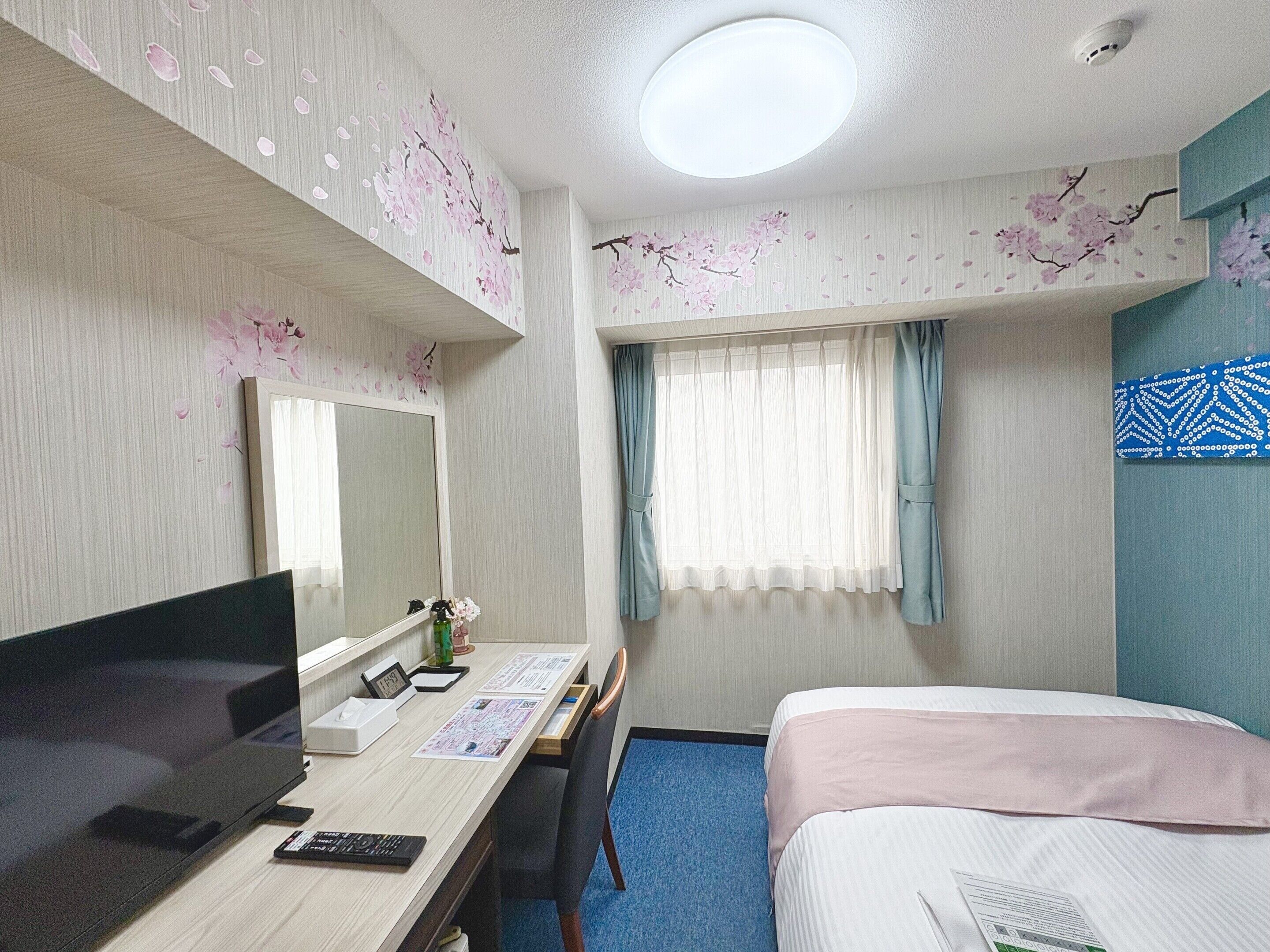 A hotel room with a bed, a desk with a computer, a TV, and a window with curtains.