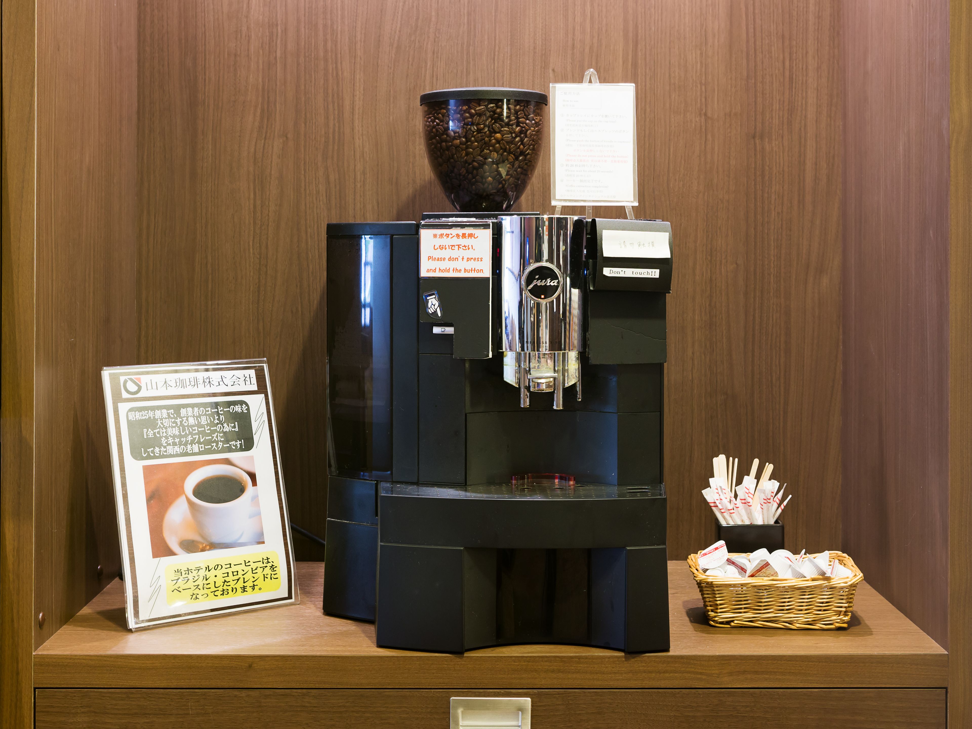 A coffee machine with a sign and a basket of napkins.