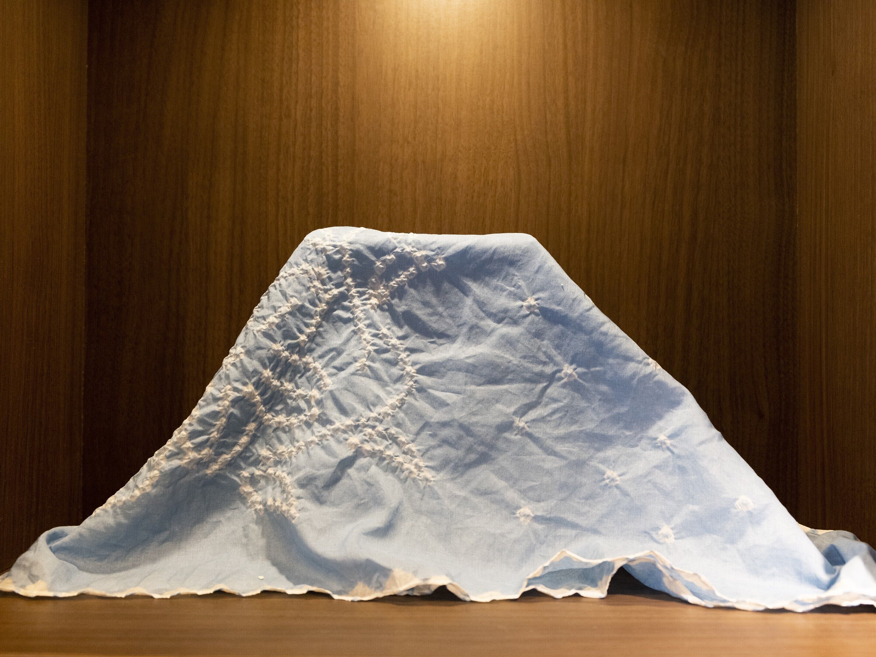 Una habitación con piso de madera y una manta blanca con textura sobre una silla.