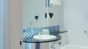 Ein modernes Badezimmer mit einem Glaswaschbecken, weißen Fliesen, einer blauen Mosaikrückwand, einer weißen Badewanne und einem Handtuchhalter.