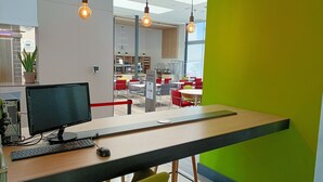 A modern office space with a computer desk, a monitor, keyboard, and mouse. There are red chairs, a green wall, and a bright window. - Holiday Inn Express Madrid-Leganes by IHG (Leganes)