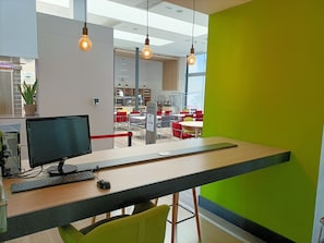 A modern office space with a computer desk, a monitor, keyboard, and mouse. There are red chairs, a green wall, and a bright window. - Holiday Inn Express Madrid-Leganes by IHG (Leganes)