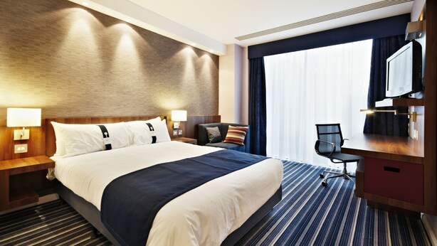 Ein Hotelzimmer mit einem großen Bett, einem Schreibtisch, einem Sessel und einem Fernseher.