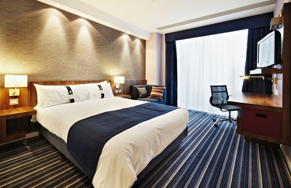 Una habitación de hotel con una cama grande, un escritorio, una silla y un televisor.