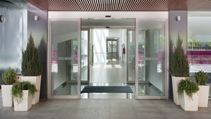 A modern building entrance with glass doors, potted plants, and a bench. - Holiday Inn Express Madrid-Leganes by IHG (Leganes)