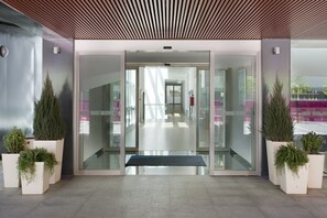 A modern building entrance with glass doors, potted plants, and a bench. - Holiday Inn Express Madrid-Leganes by IHG (Leganes)