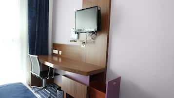 A hotel room with a wooden desk, a chair, a flat-screen TV, and a small storage space.
