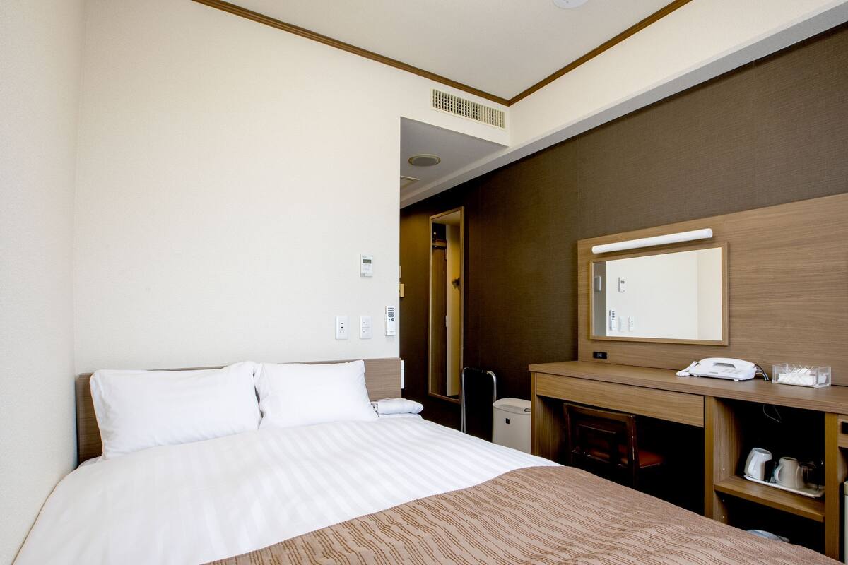 A hotel room with a bed, a desk, a mirror, and a telephone.