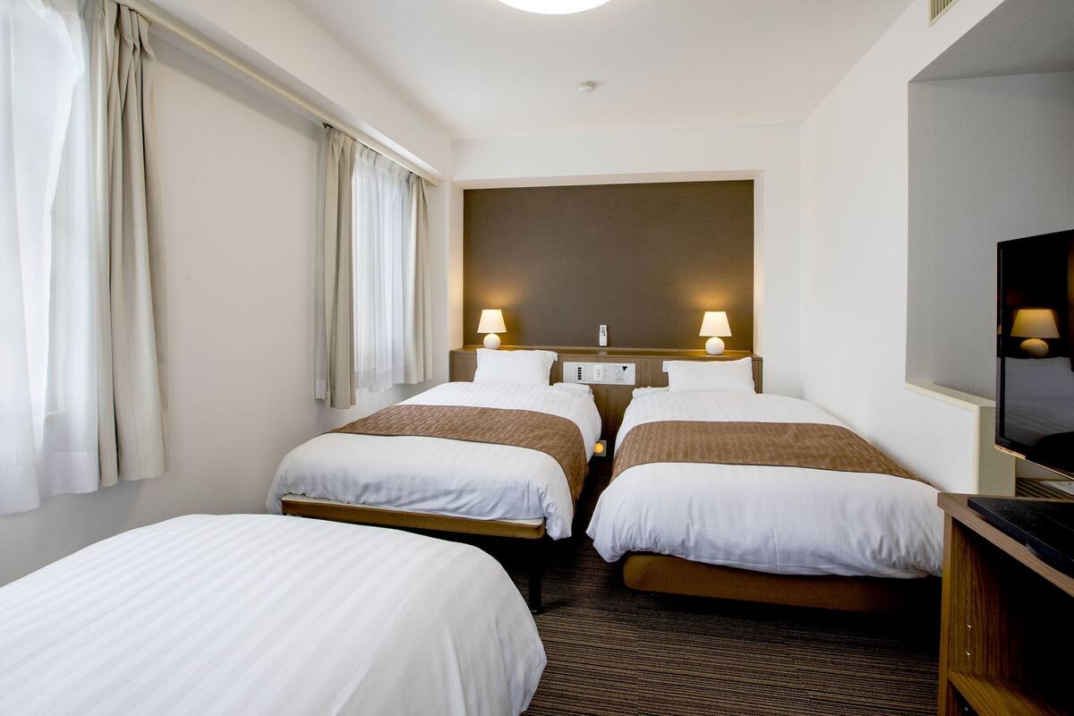 A hotel room with two beds, a large mirror, a flat-screen TV, and a ceiling light.