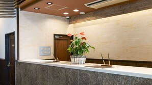 A reception area with a marble counter, a potted plant with red flowers, a sign with room numbers, and a wooden door. - KOKO STAY Hitachi (Hitachi)