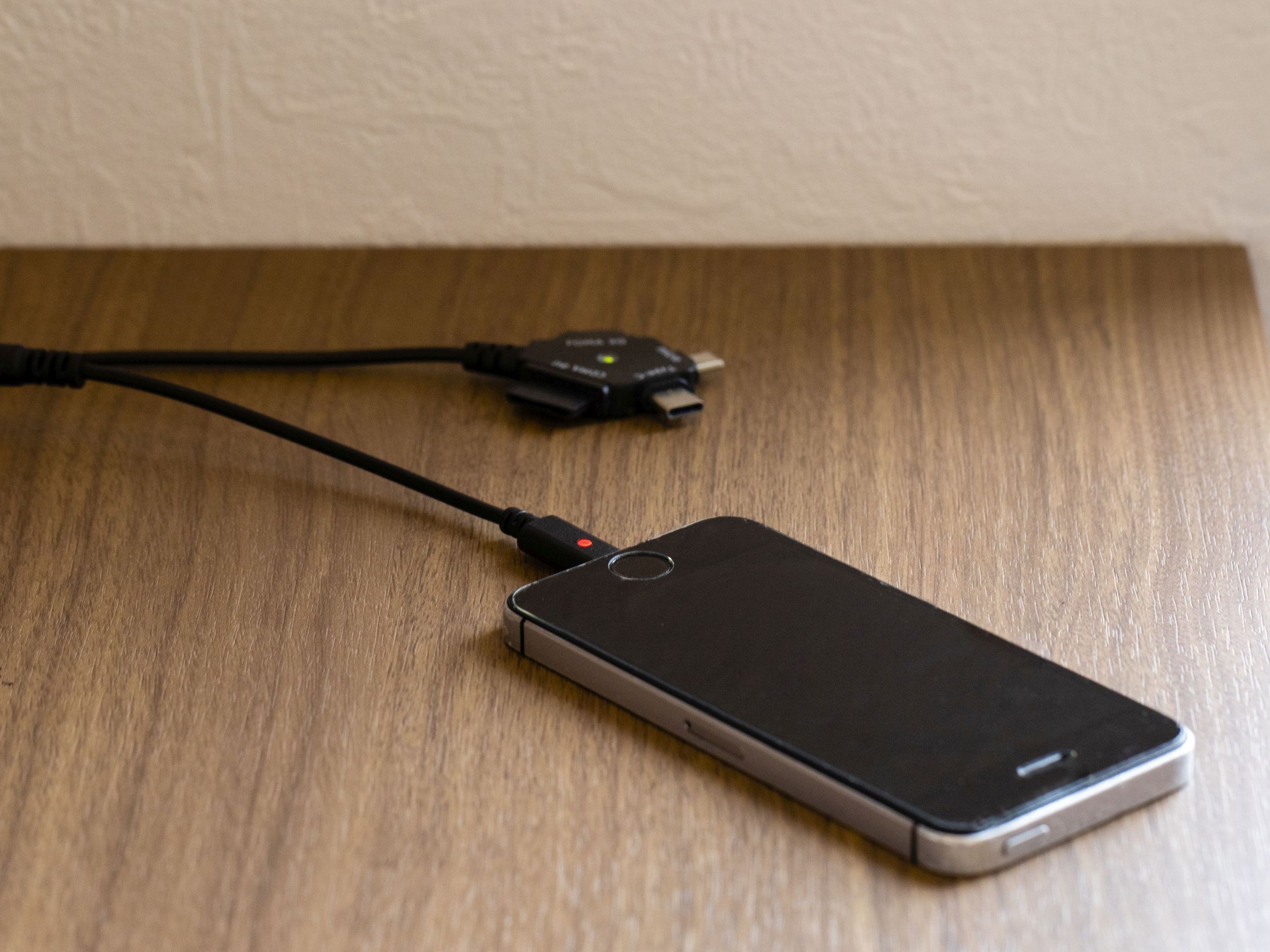A smartphone connected to a charger on a wooden surface.