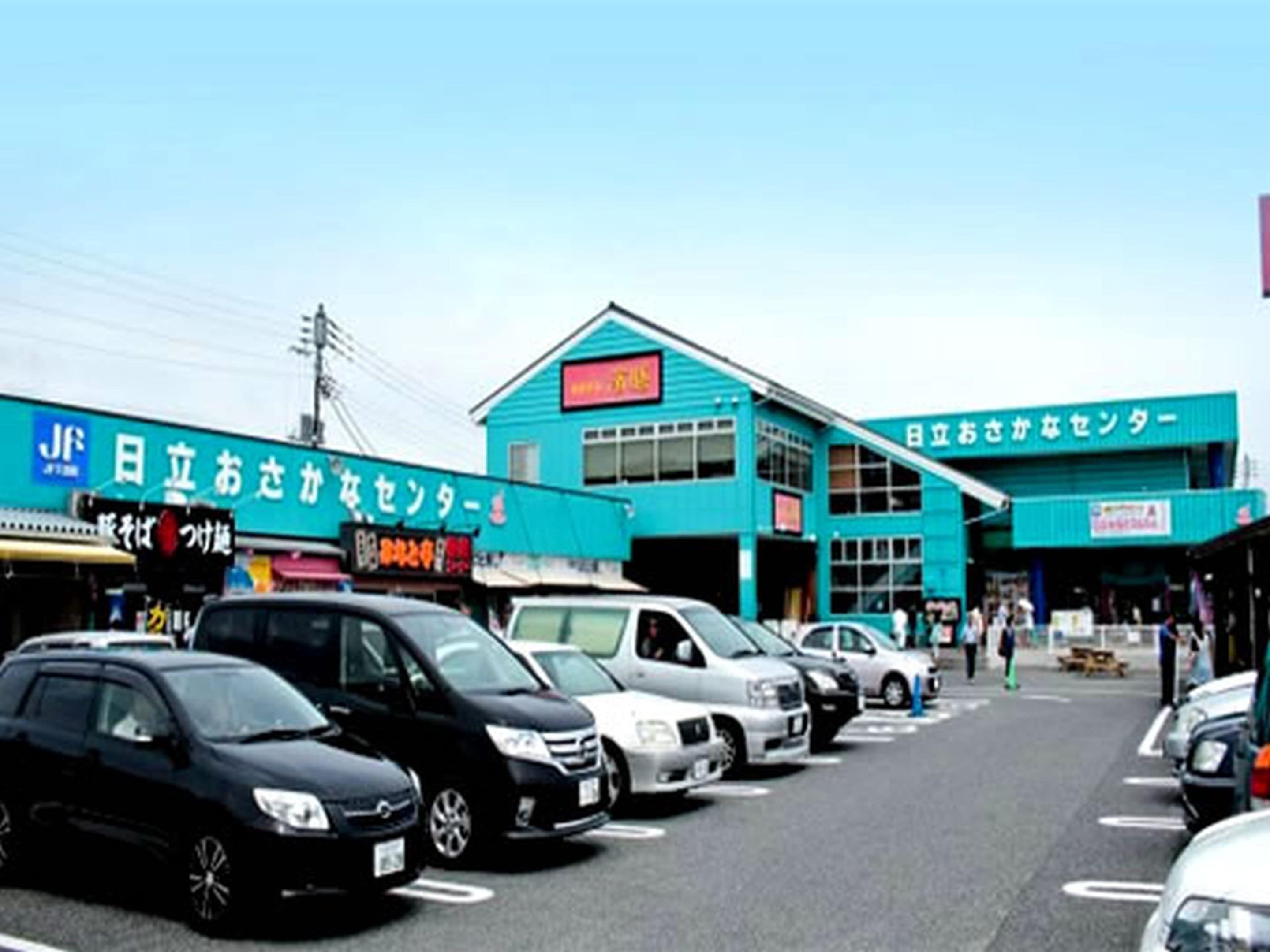 A parking lot with several cars parked in front of a building with a blue facade and signage in a foreign language.