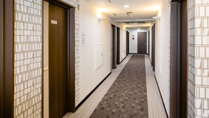 A hotel hallway with a carpeted floor, wooden doors, and a tiled wall pattern. - KOKO STAY Hitachi (Hitachi)