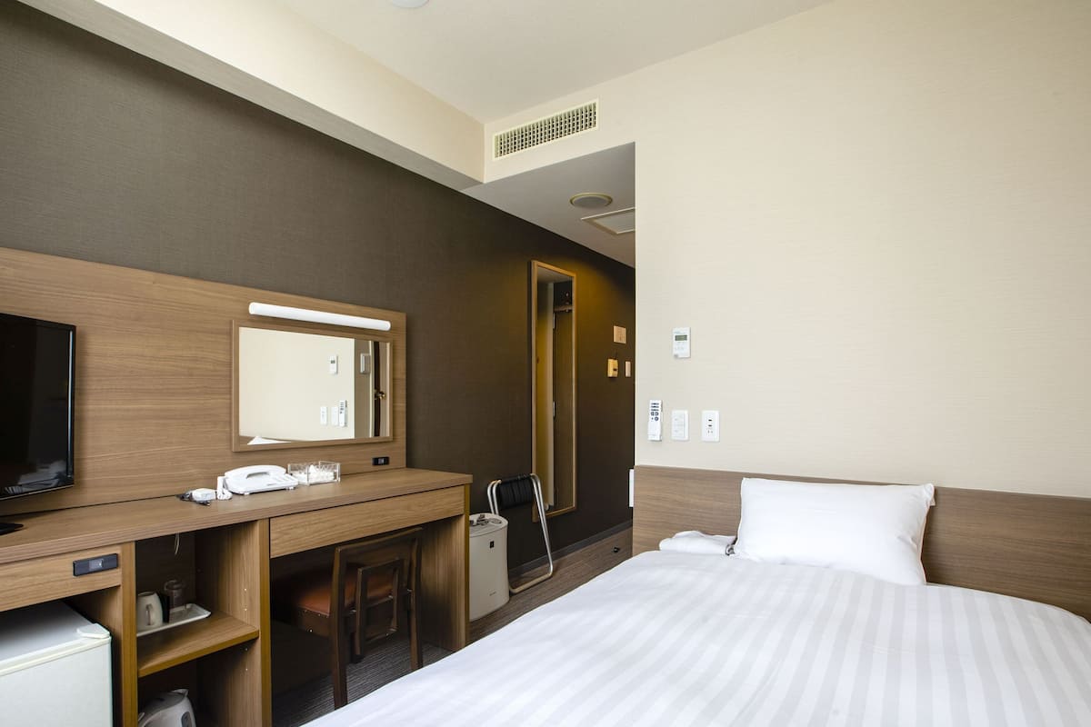 A hotel room with a bed, a desk with a mirror, a television, a coffee maker, and a telephone.