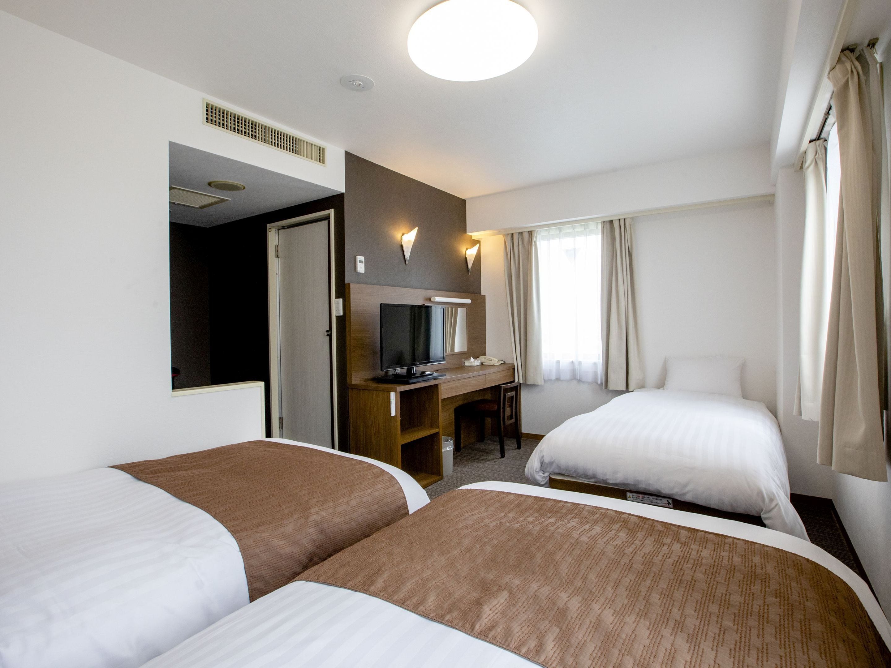Habitació d'hotel amb dos llits, una taula amb televisió, un mirall i una finestra amb cortines.