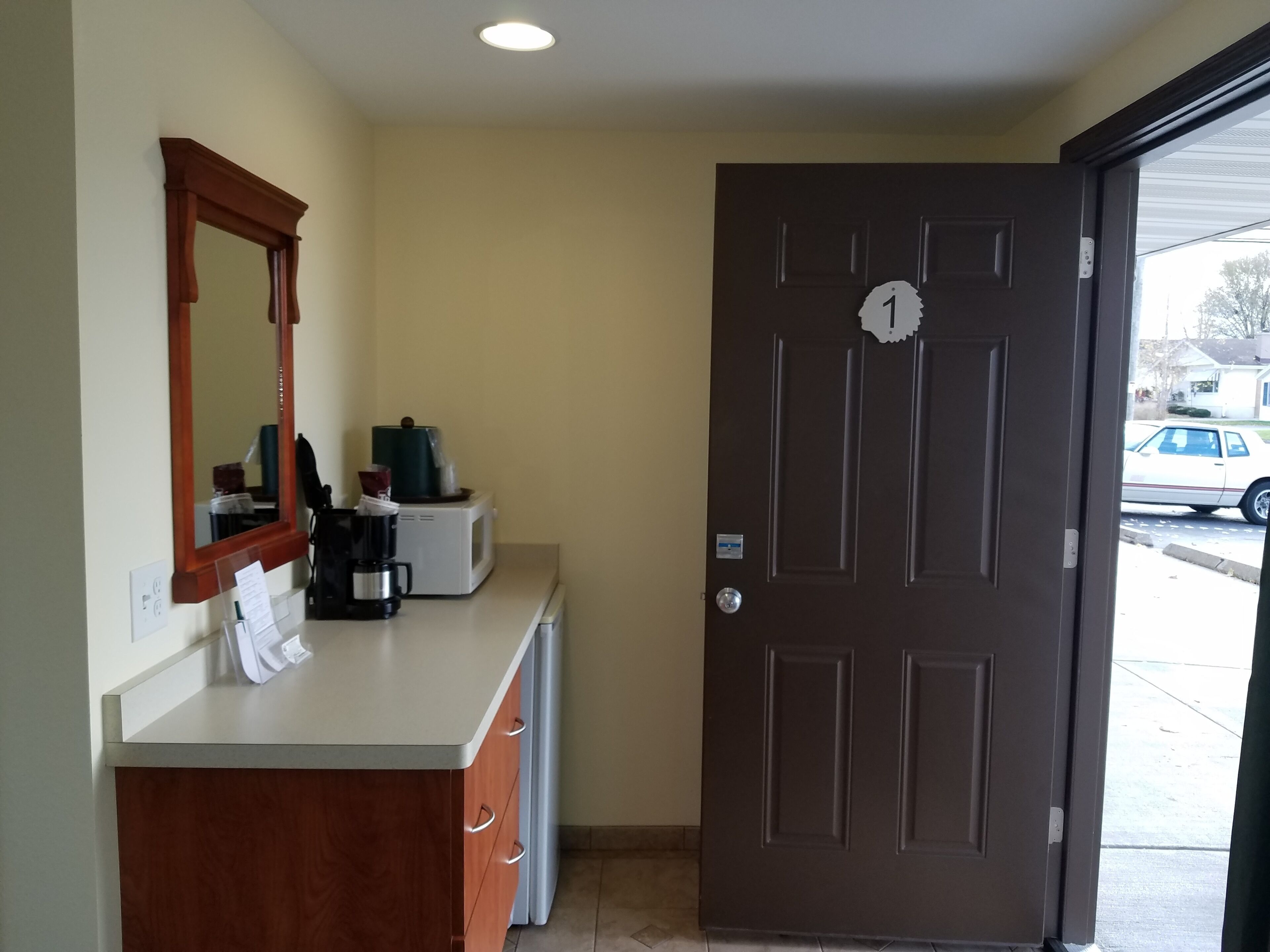 Habitación de hotel con tocador de madera, espejo, microondas y una puerta con un número.