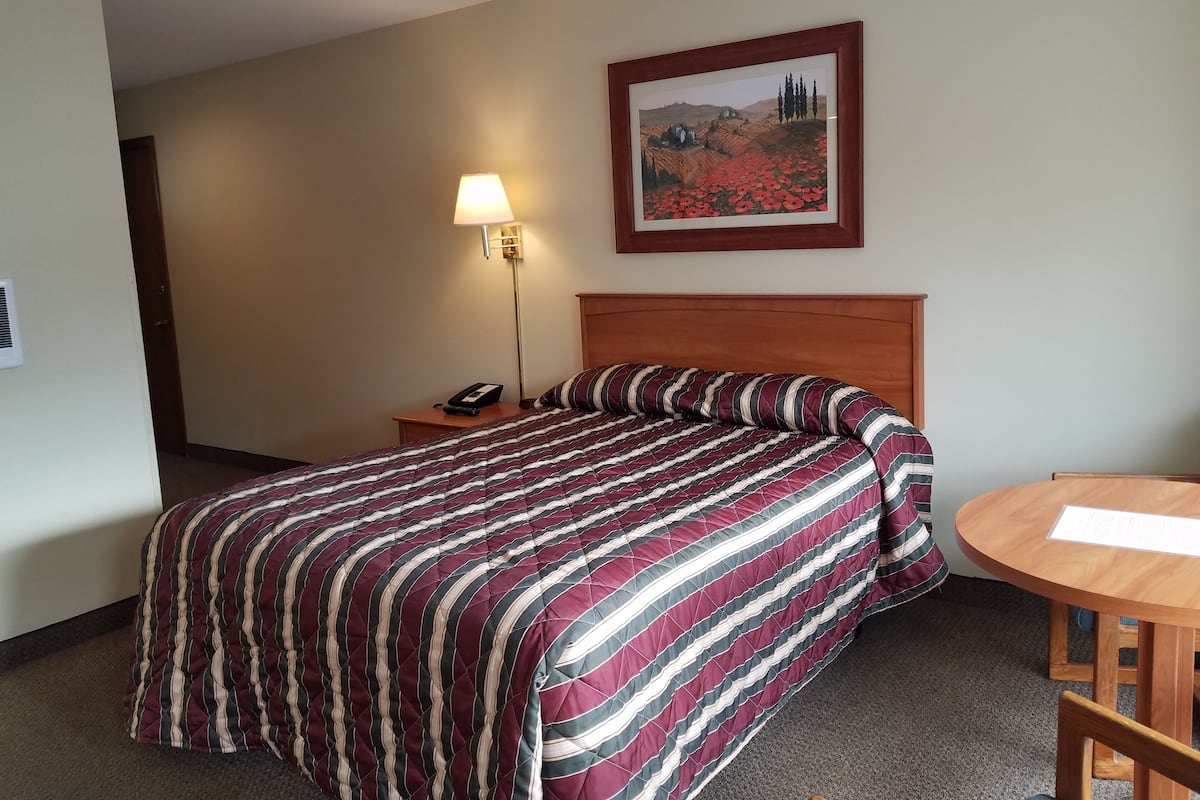 A hotel room with a bed, a bedside table with a lamp, a framed picture on the wall, and a small round table with a menu.