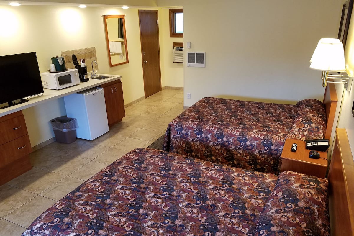 A hotel room with two beds, a desk with a TV, a microwave, and a small refrigerator.