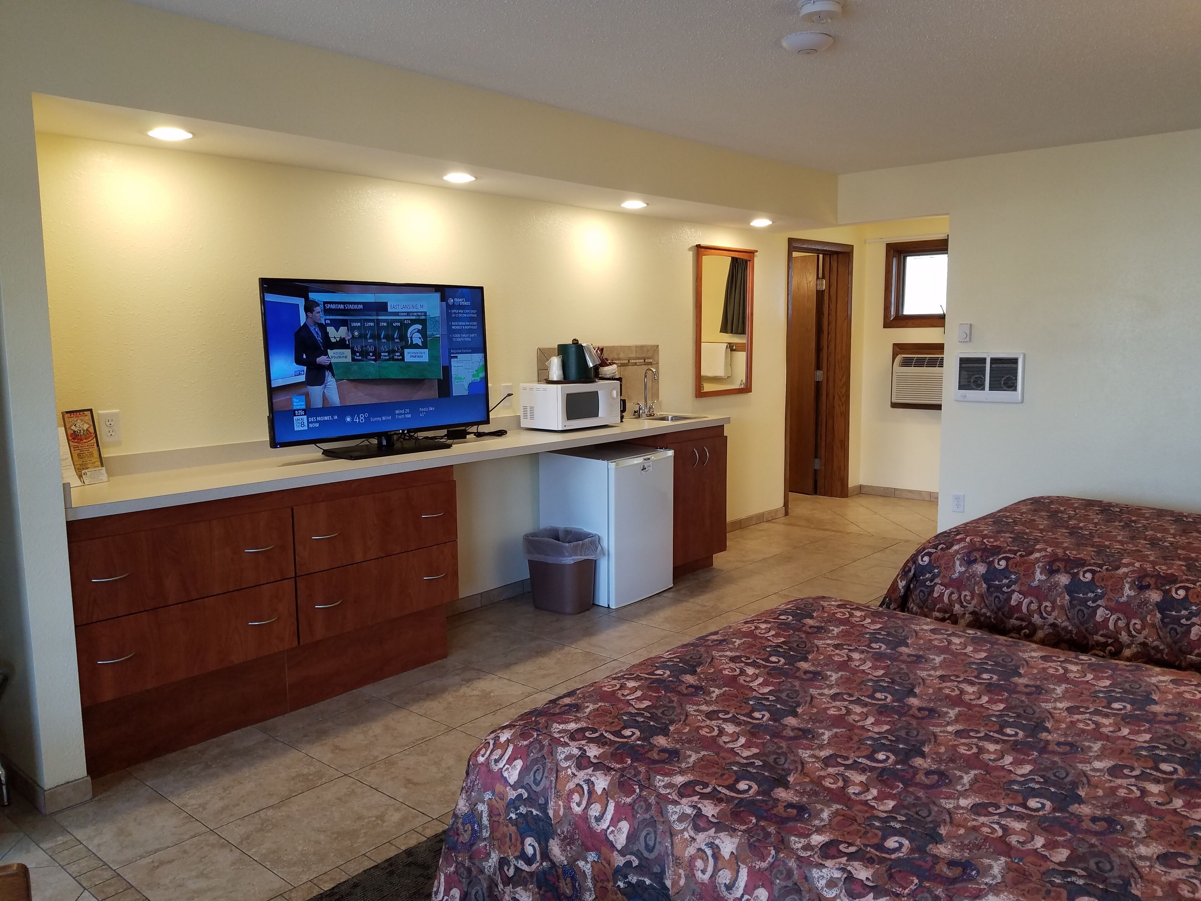 Habitación de hotel con cama, escritorio con televisor, microondas y cesto de basura.