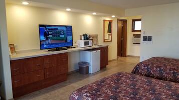 Habitación de hotel con cama, escritorio con televisor, microondas y cesto de basura.