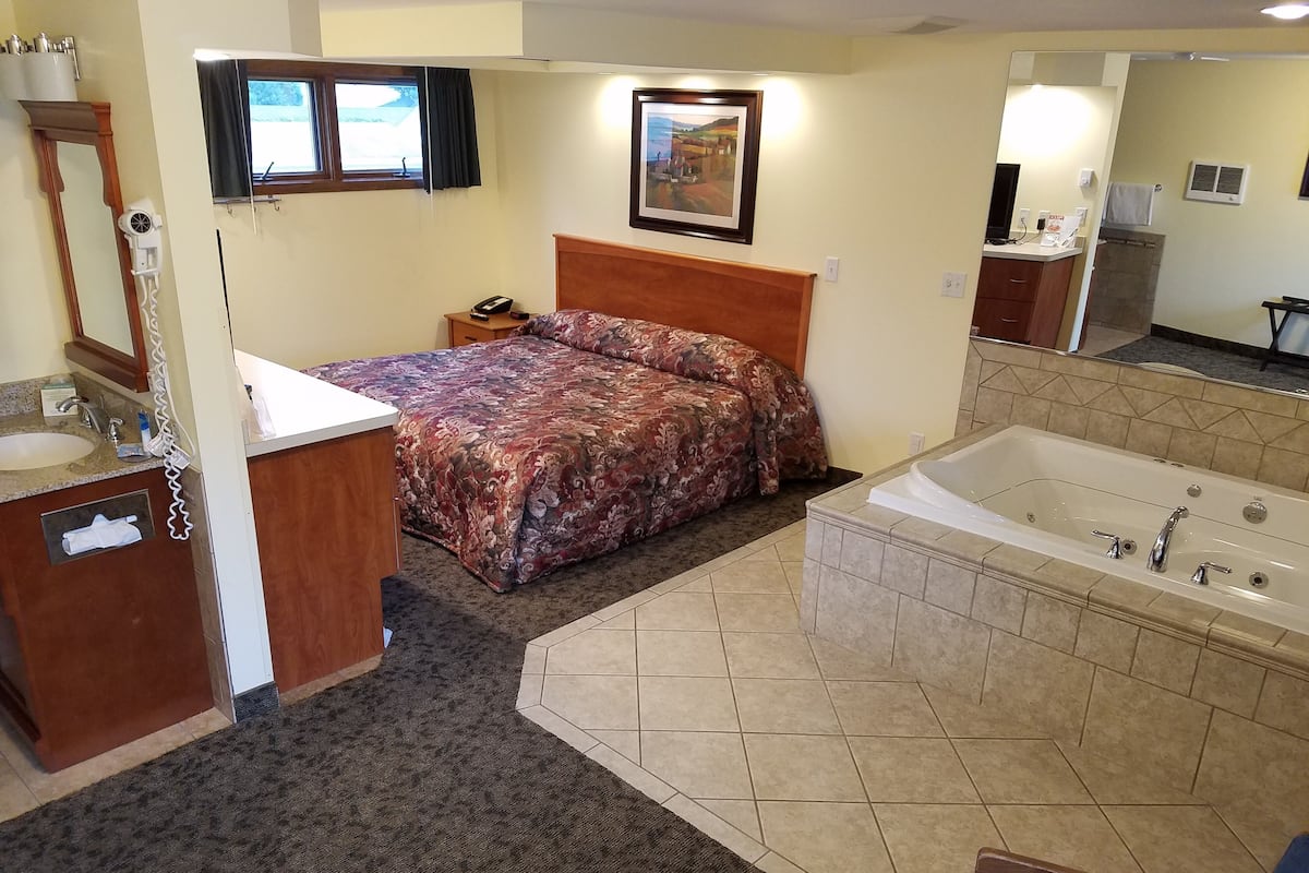 A hotel room with a bed, a bathroom with a bathtub, a sink, and a mirror.