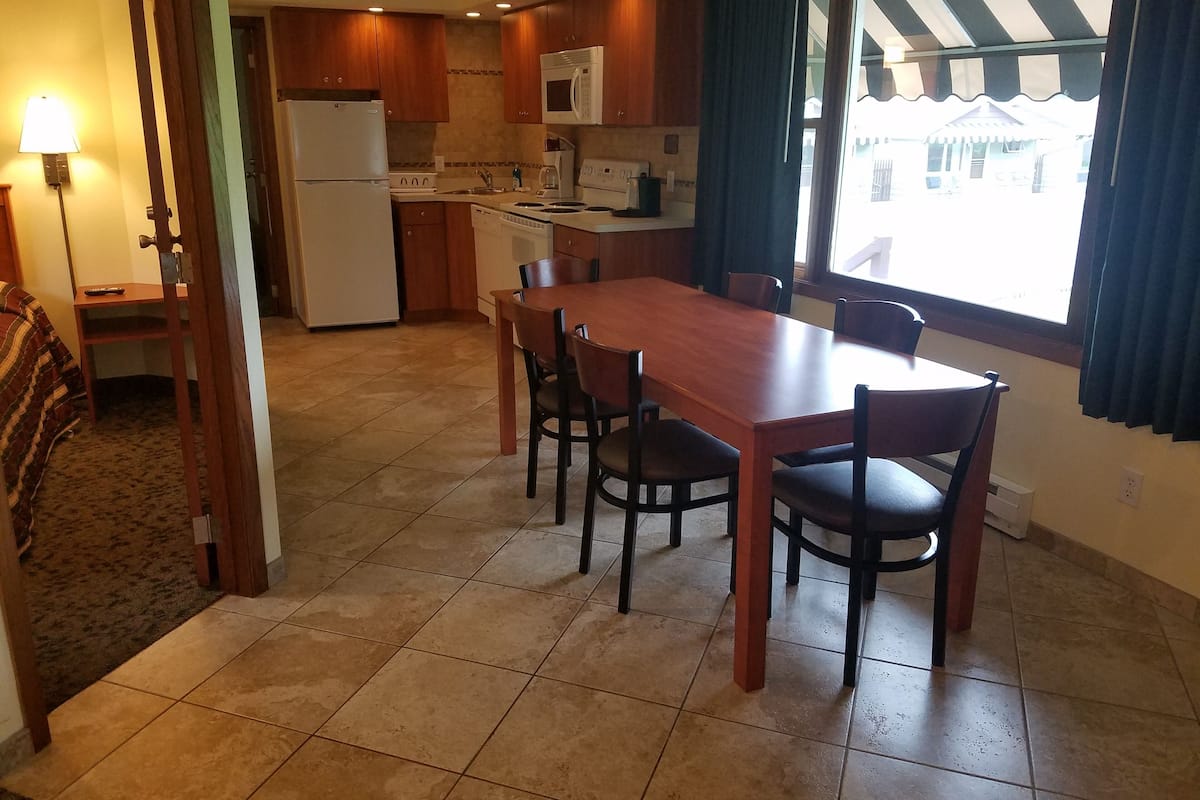 A compact kitchen with wooden cabinets, a white refrigerator, a microwave, and a dishwasher. There is a dining table with four chairs.