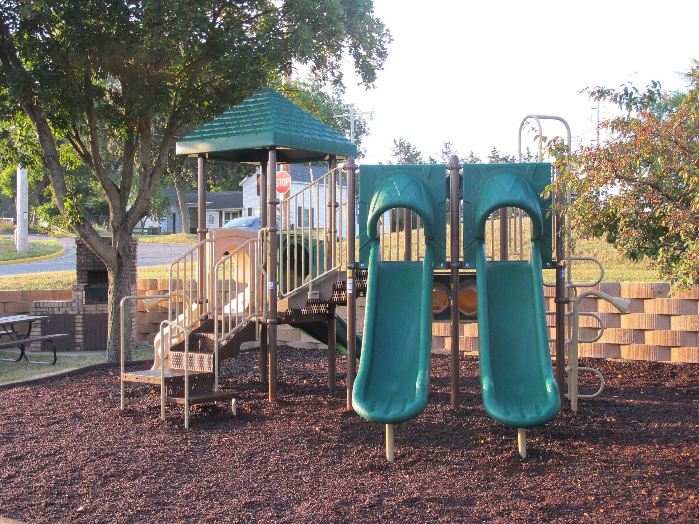 A playground with two slides, a climbing structure, and a covered playhouse.