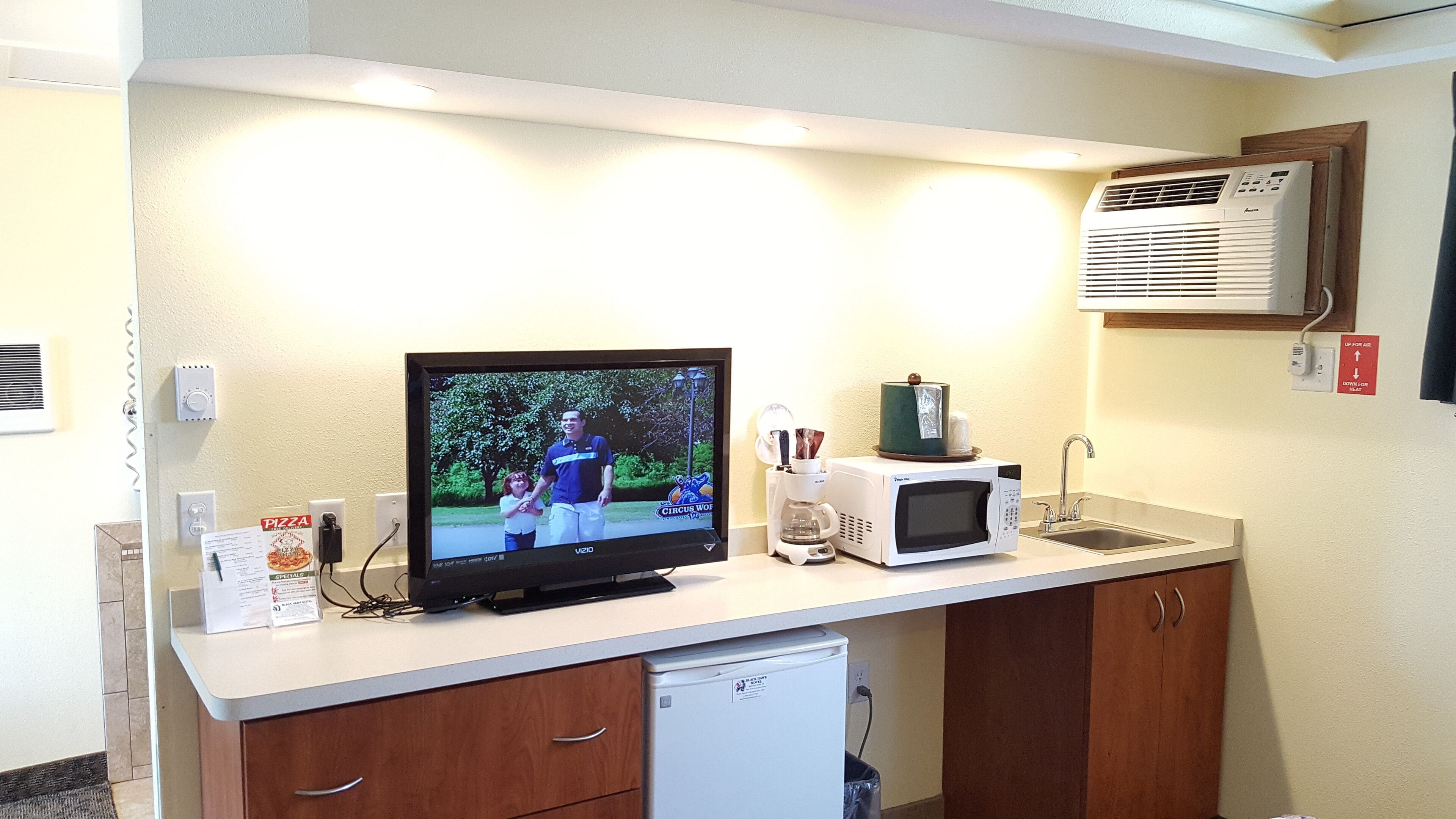 Una kitchenette equipada con televisor, microondas, cafetera y un refrigerador pequeño.