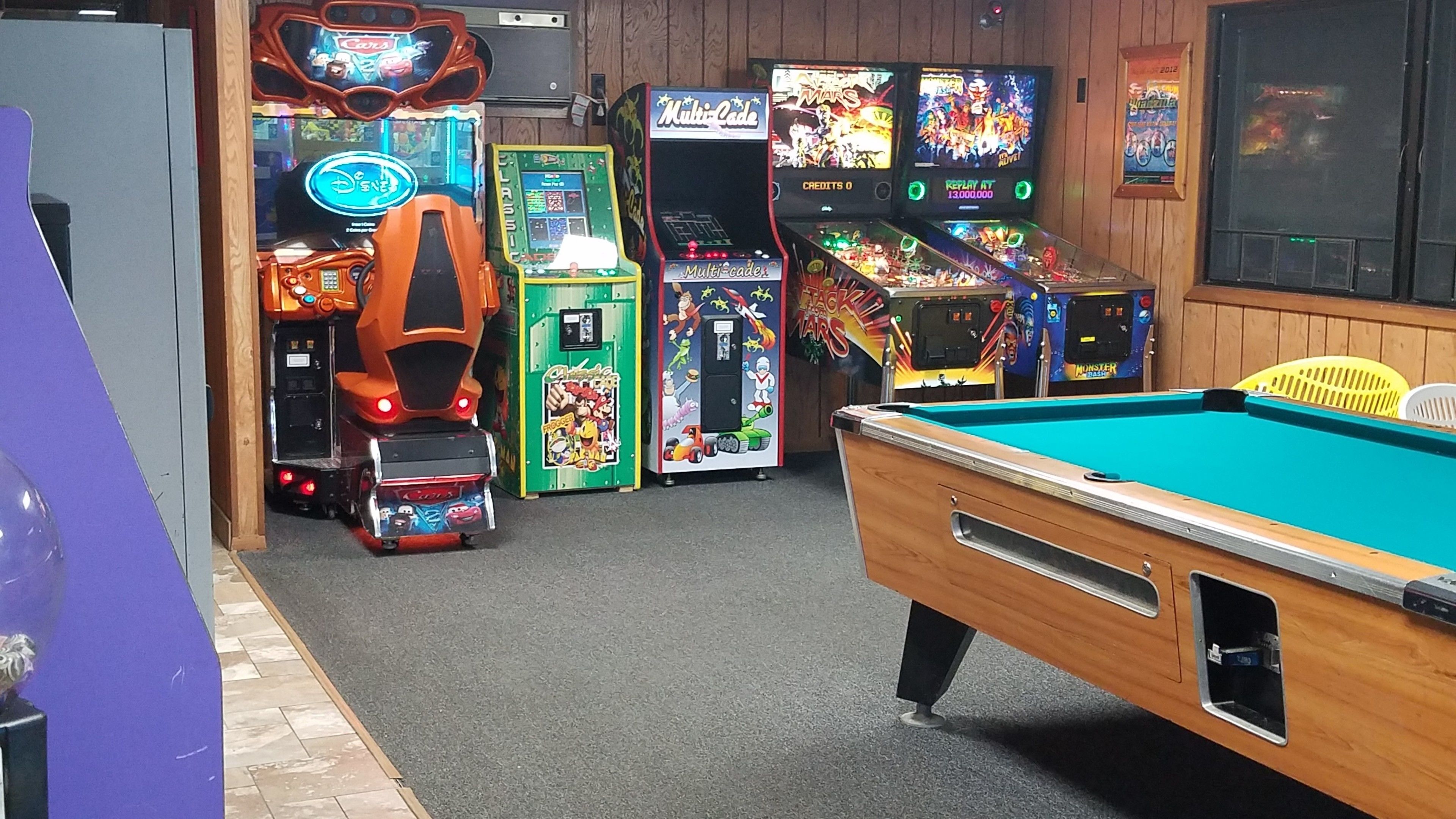 Una habitación con mesa de billar, juegos de arcade y pared de madera.