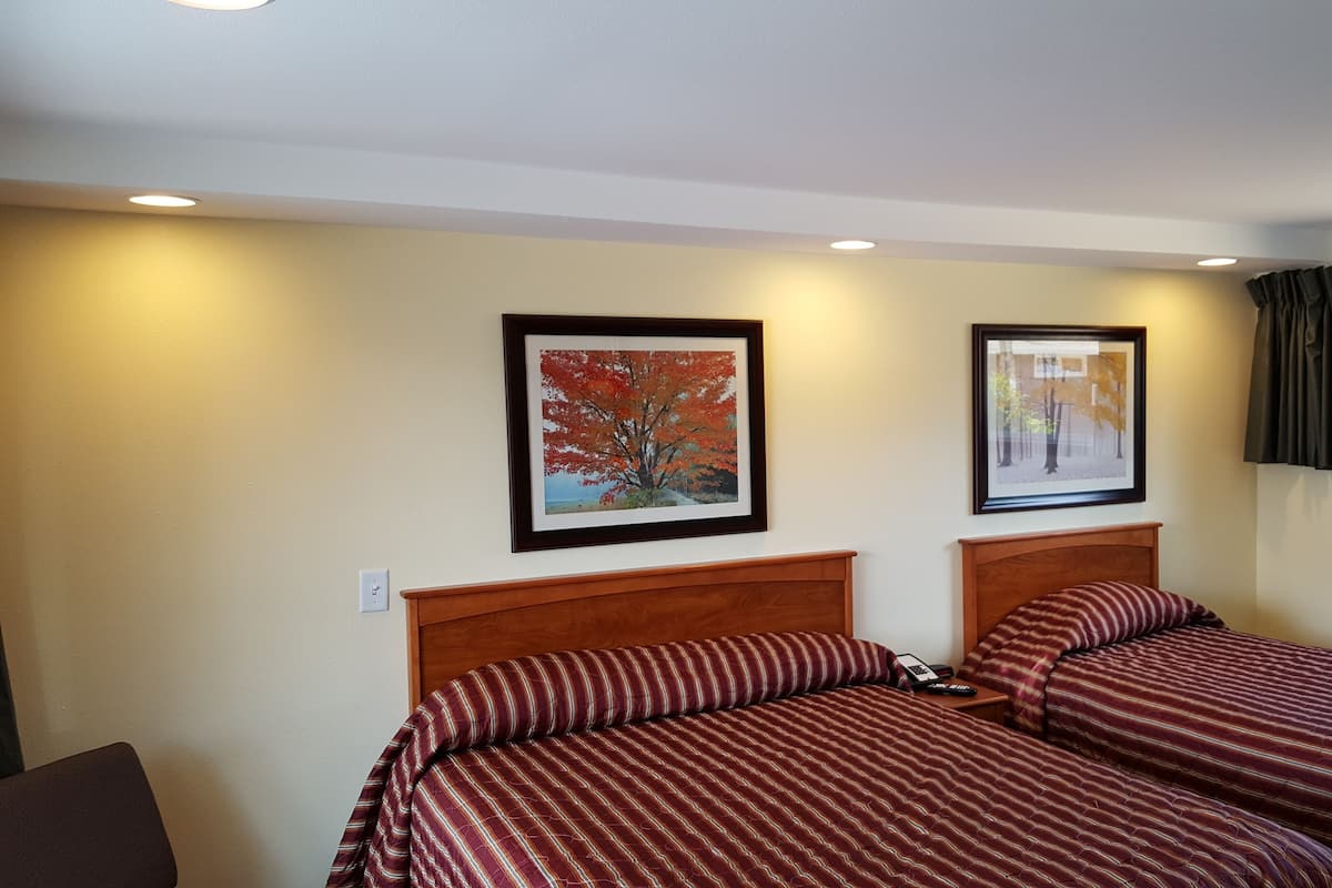 A hotel room with two beds, each with striped bedding, a wooden headboard, and framed pictures on the wall.