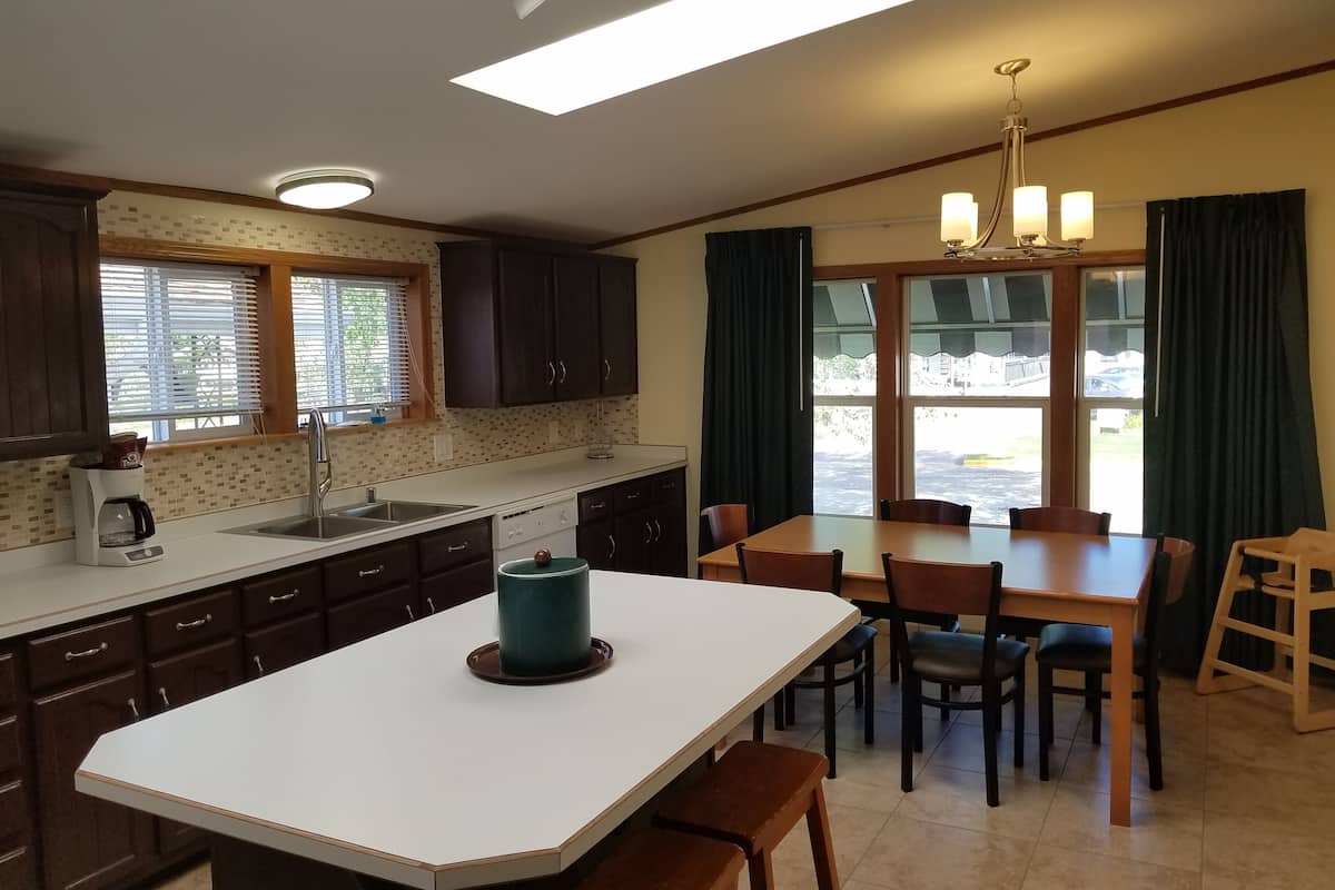 A modern kitchen with a central island, a dining area with a table and chairs, and large windows with curtains.