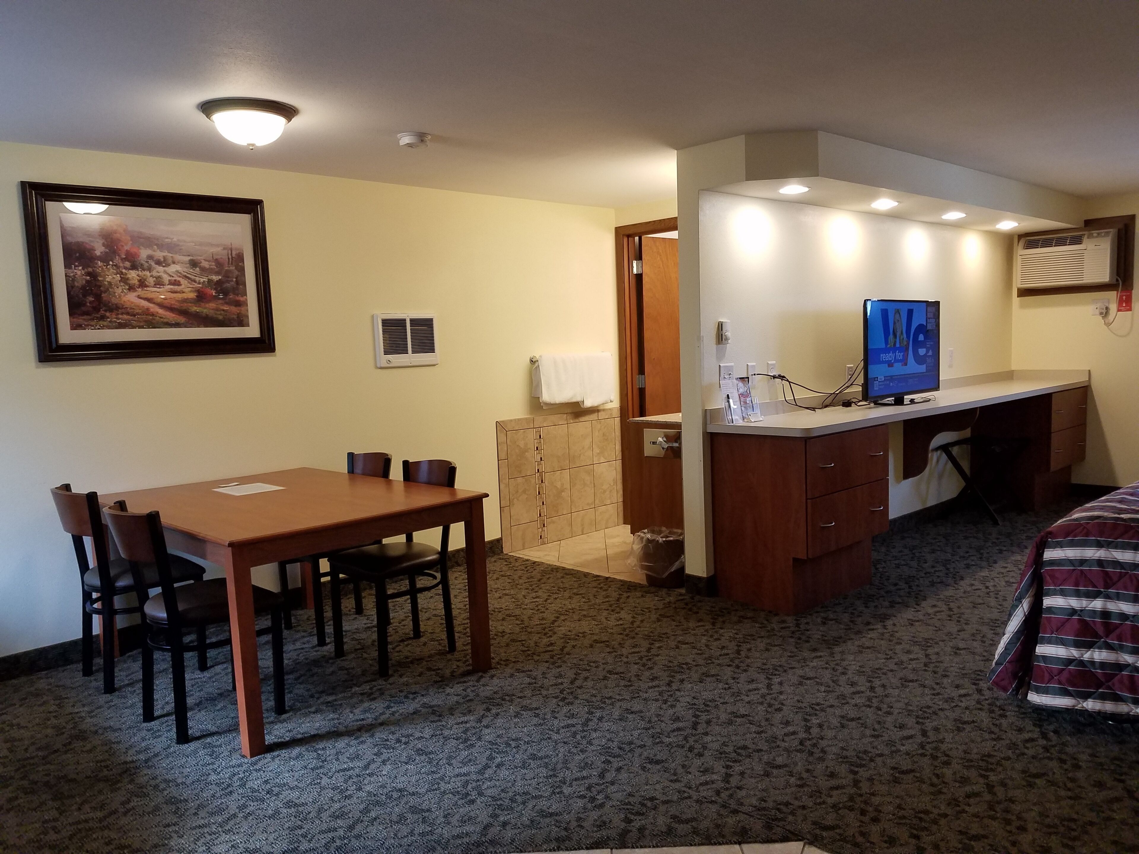 Habitación de hotel con mesa de comedor y sillas, una pequeña kitchenette, cama y un cuadro en la pared.