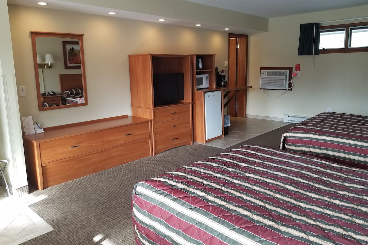 A hotel room with a wooden dresser, a television, a microwave, a refrigerator, a bed with striped bedding, a mirror, and a window with curtains.