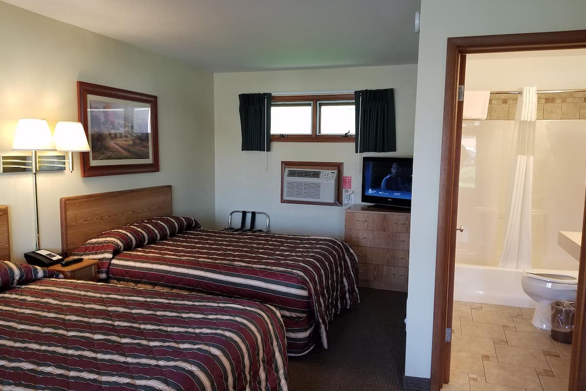 A hotel room with two beds, a TV, a desk, and a bathroom.