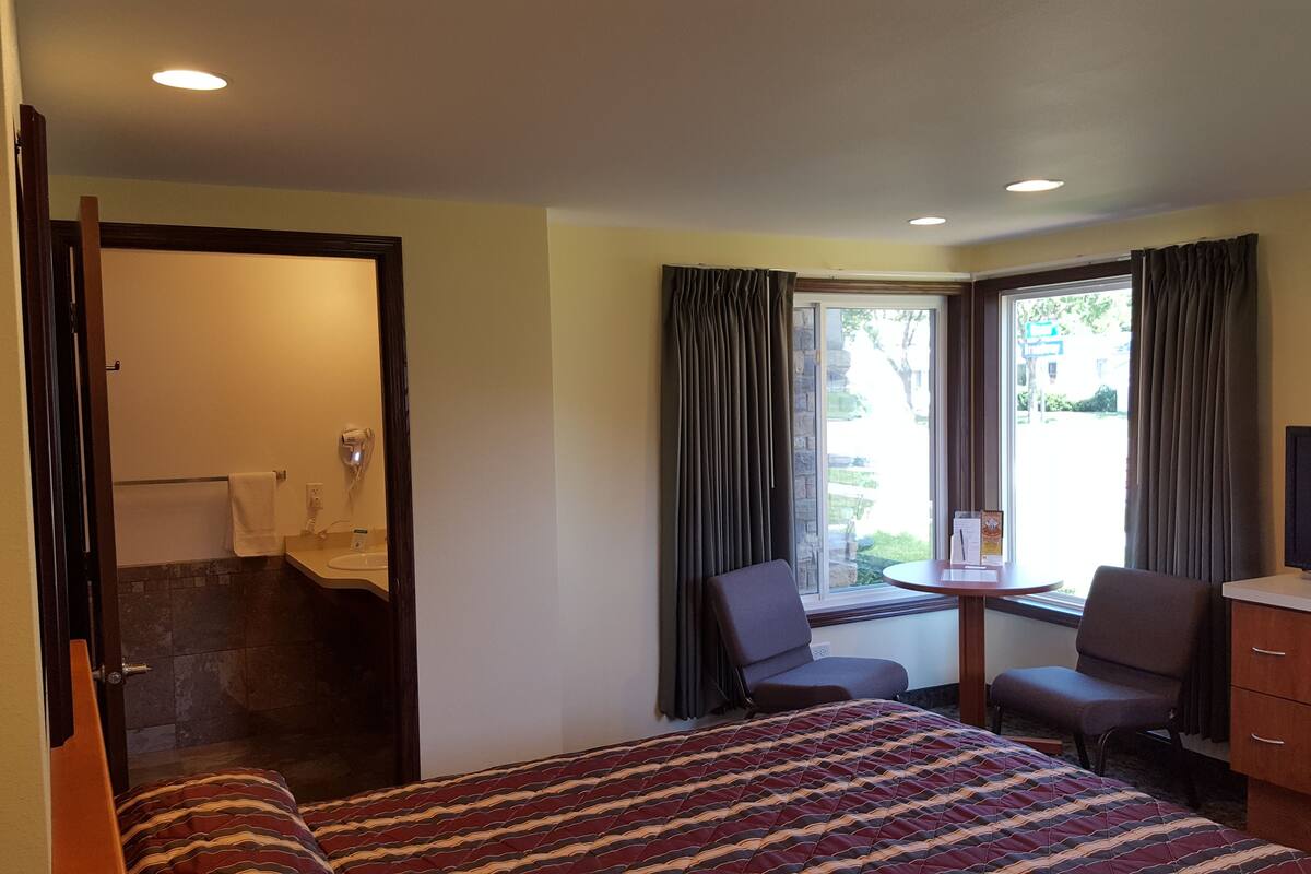 A hotel room with a bed, a TV, a desk, and a window with curtains.